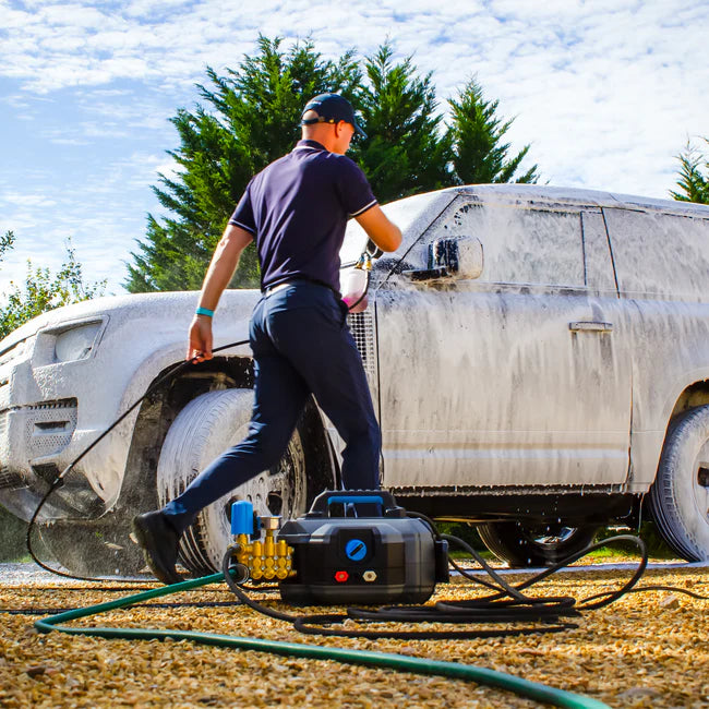 Person using a pressure washer on a vehicle outdoors
