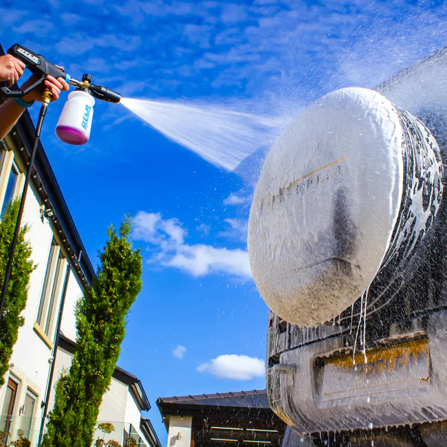 Person using a pressure washer to clean a large spherical object against a blue sky.